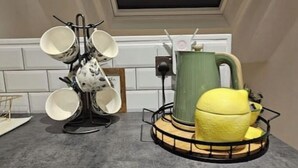 A kitchen with a coffee maker, a kettle, and a fruit bowl on the counter. - Stylish 2-Bed Apartment in the Heart of Windsor – Walk to Windsor Castle (Windsor)