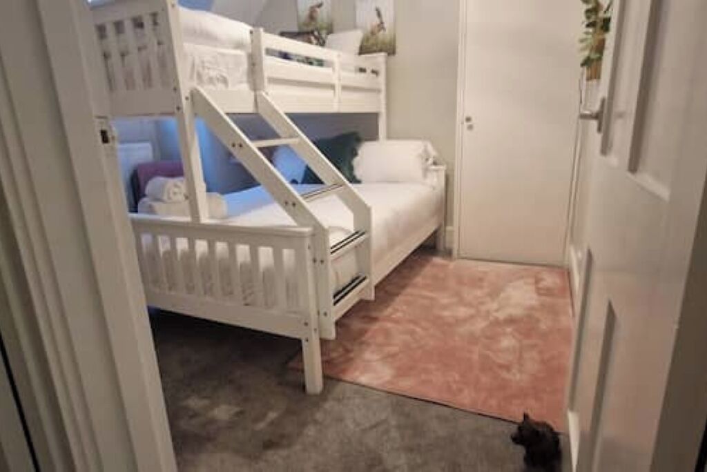 A bunk bed room with a staircase, a small bedside table, and a door.
