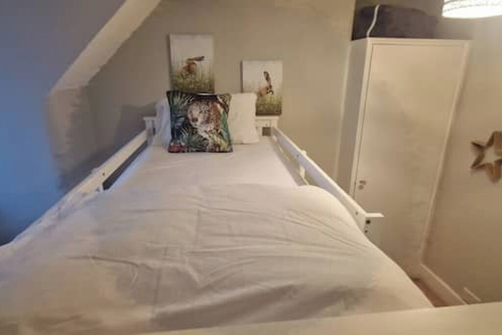 Une petite pièce avec un lit simple, une petite table et deux tableaux accrochés au mur.