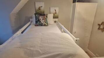 Une petite pièce avec un lit simple, une petite table et deux tableaux accrochés au mur.