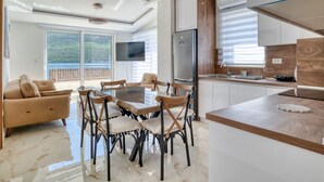 A modern kitchen with a central island, a dining area with a glass table, and a living space with a sofa and a TV. - Ljubica Superior 3-Zimmer-Apartment mit Meerblick by Interhome (Herceg Novi)