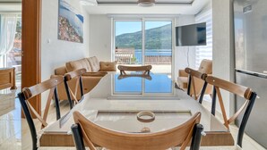 A modern dining area with a large table, chairs, and a view of a mountainous landscape through large windows. - Ljubica Superior 3-Zimmer-Apartment mit Meerblick by Interhome (Herceg Novi)