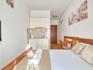 Une chambre d’hôtel avec un lit, une chaise en bois, une petite table, un coin cuisine et un tableau accroché au mur.