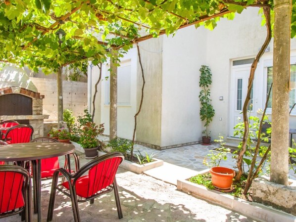 An outdoor patio with a stone oven, red chairs, and potted plants.