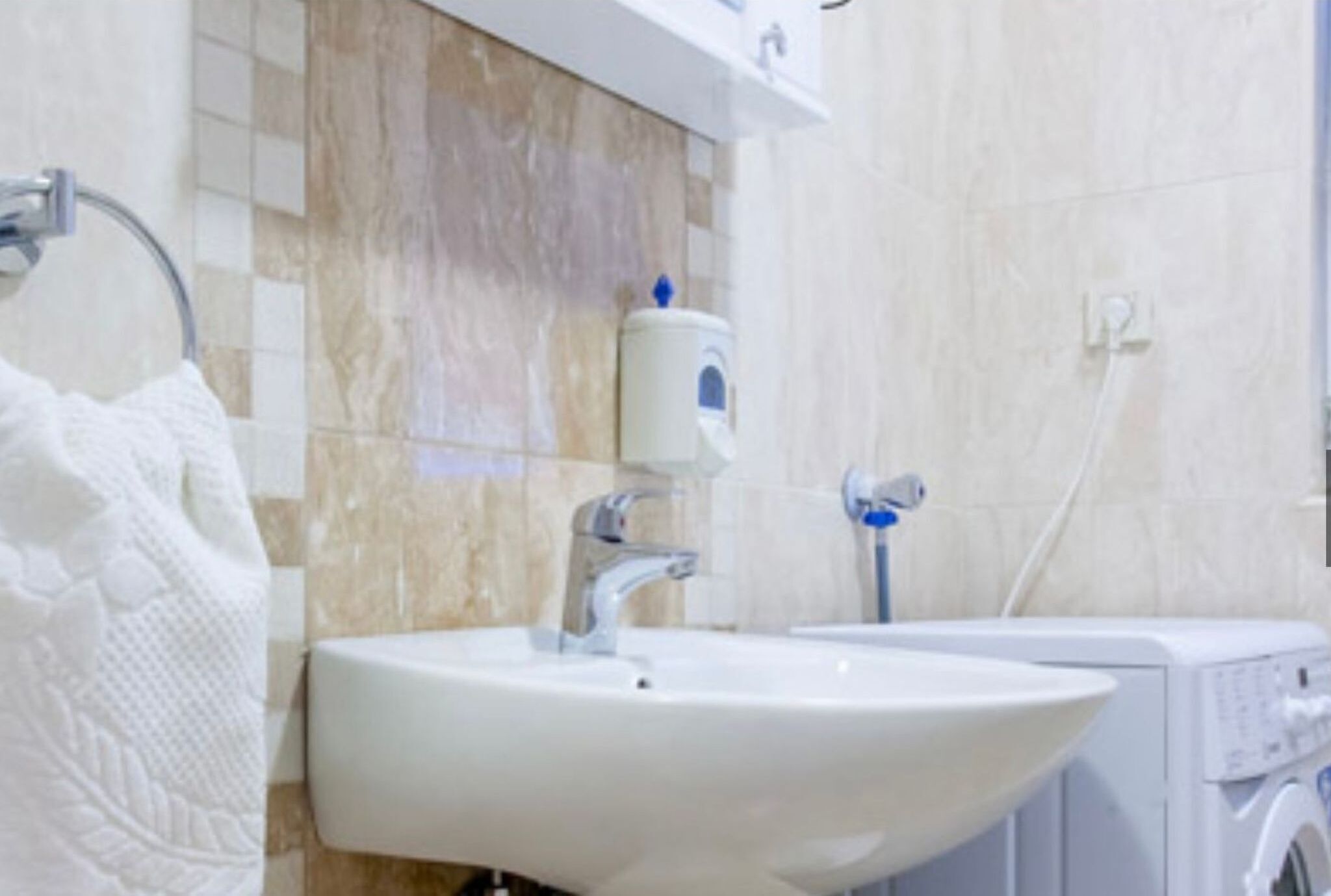 Une salle de bain avec un lavabo blanc, un porte-serviettes, un distributeur de savon et un lave-linge.
