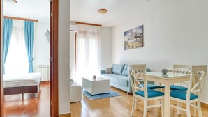 A modern living room with a sofa, a dining table with chairs, and a bed in the adjacent room. - Wohnung "Premier" mit Meerblick by Interhome (Herceg Novi)