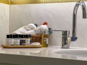 Casa de banho com lavatório moderno, um frasco de óleo de banho e uma cesta de produtos de higiene pessoal.