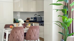 A modern kitchen with white cabinets, a dining area with a marble table and brown upholstered chairs, and a large green plant. - Qoople Aria-07 neue Wohnung im Stadtzentrum by Interhome (Alanya)