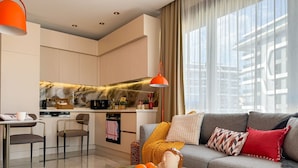 Een moderne woonkamer met een grijze bank, een glazen salontafel en een keuken op de achtergrond.