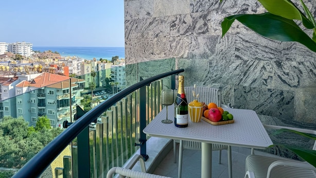 Een balkon met een tafel, een fles champagne en een schaal met fruit.