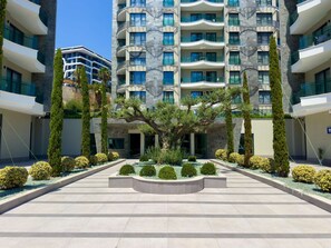 A modern multi-story hotel with a central courtyard featuring neatly trimmed bushes and a large tree. - Qoople Eхсellence B-19 neue Wohnung am Meer by Interhome (Alanya)