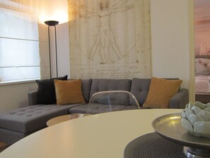 Un salon moderne avec un canapé d’angle gris, une table basse ronde et un grand tableau abstrait accroché au mur.
