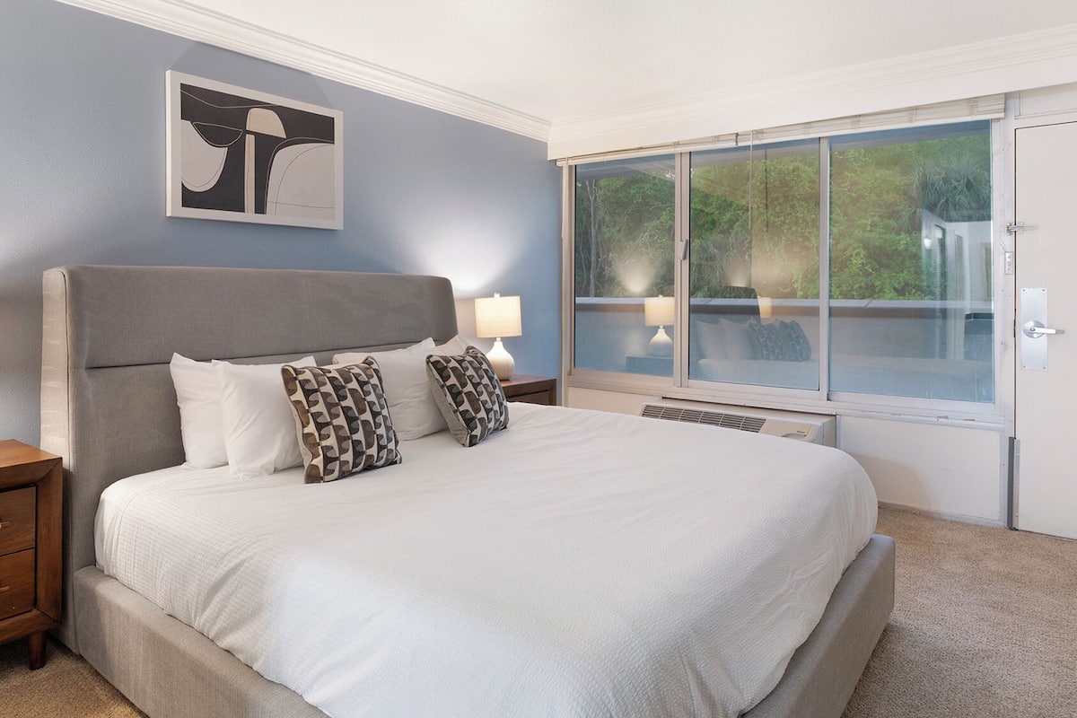 A bedroom with a bed, nightstands, a window, and a painting on the wall.