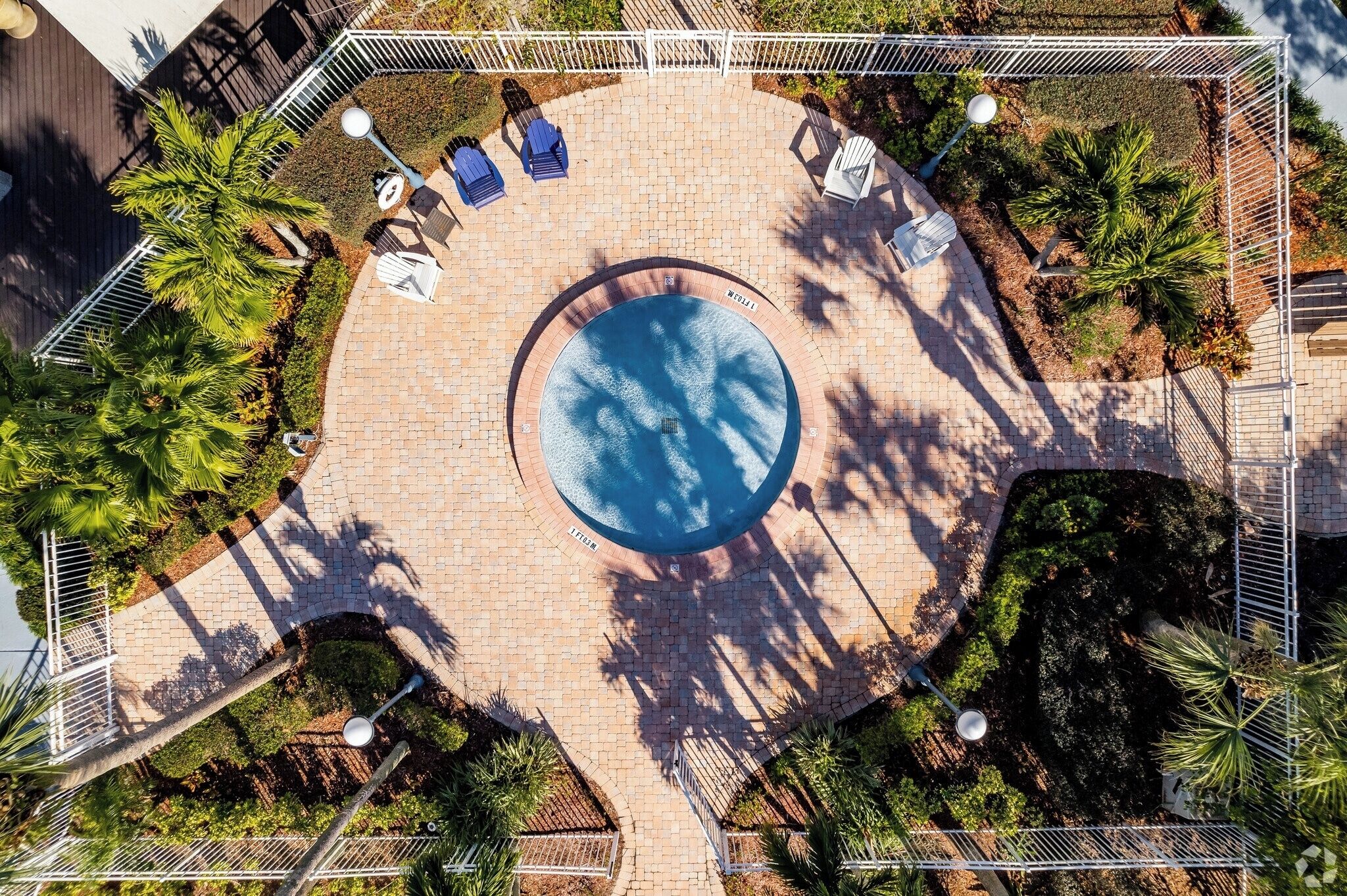 An aerial view of a circular pool surrounded by a paved patio with lounge chairs and palm trees.