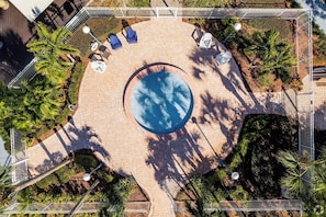 An aerial view of a circular pool surrounded by a paved patio with lounge chairs and palm trees.