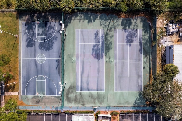 An aerial view of a tennis court with surrounding greenery and a parking lot.
