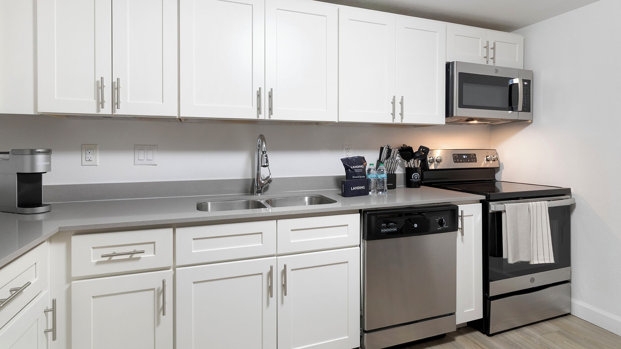 Una cocina moderna con armarios blancos, electrodomésticos de acero inoxidable, lavavajillas y microondas.