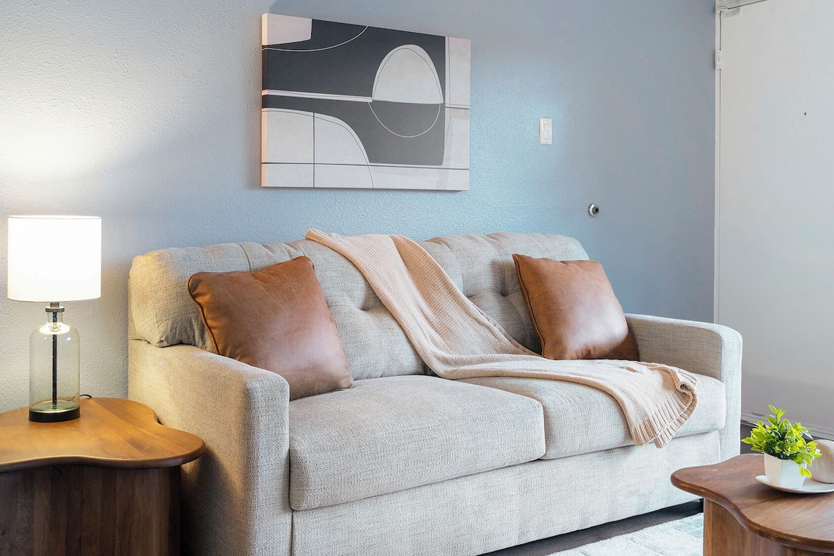 A living room with a sofa, a lamp, a painting, and a small table with a plant.