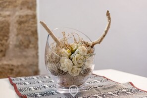 A clear glass vase with dried branches and white flowers on a patterned tablecloth. - Delì Apartment – Your cozy retreat in the heart of Alghero (Alghero)