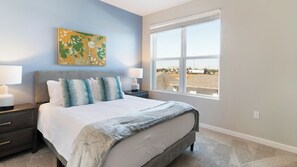 A bedroom with a bed, two bedside tables with lamps, a large window with a view, and a painting on the wall. - Landing Furnished Apartments Davenport near Northeast Regional Park (Davenport)