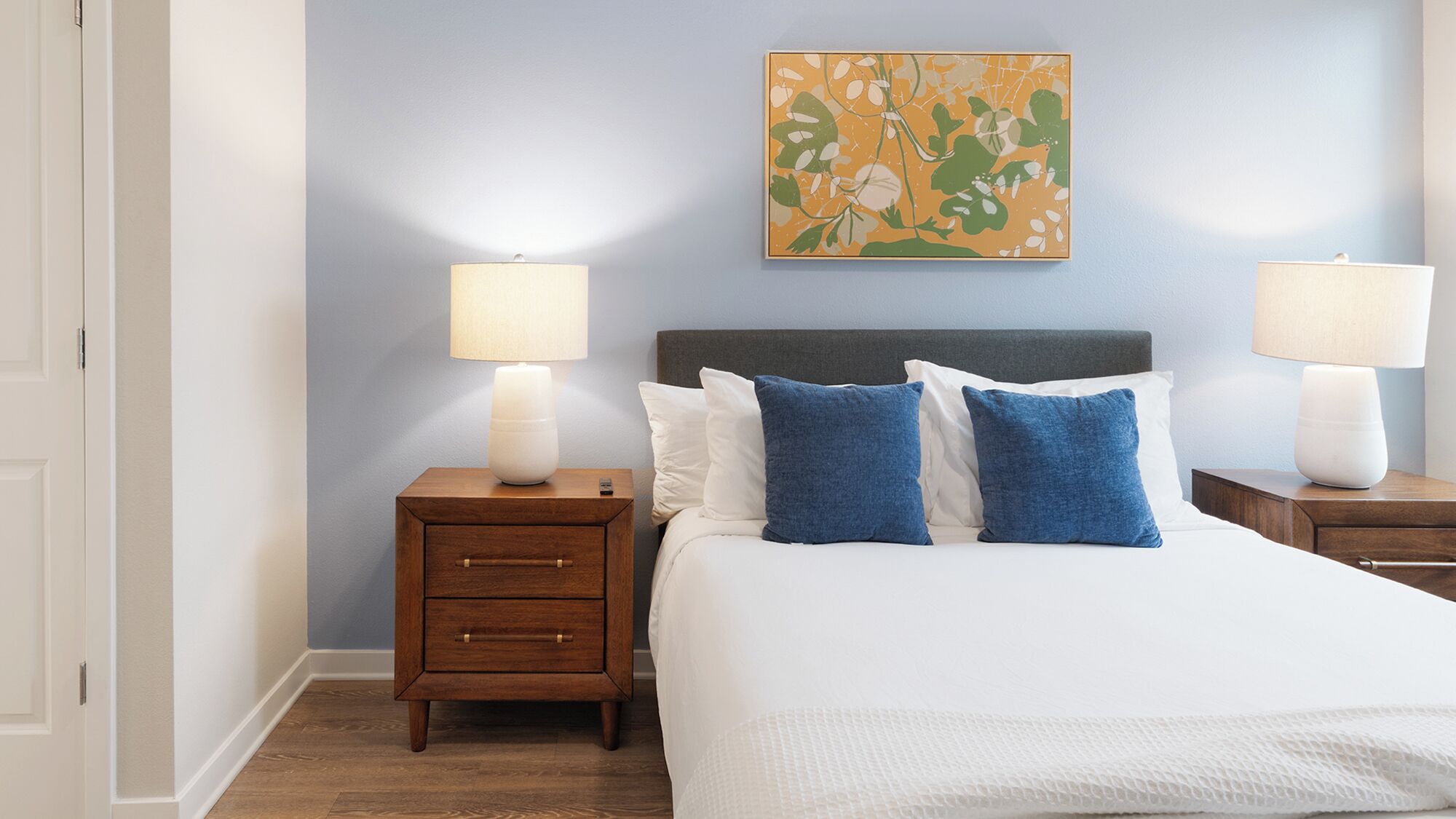 Un dormitorio ordenado con una cama, dos mesitas de noche y dos lámparas de pared.