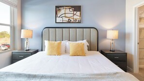 A hotel room with a large bed, two bedside tables with lamps, a headboard, and a painting on the wall. - Landing Furnished Apartments Davenport near Northeast Regional Park (Davenport)