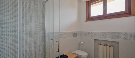 A bathroom with a glass shower enclosure, a wooden bench, a toilet, and a window.