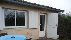 A house with a patio area featuring a blue table and two chairs, a white door, and a window with shutters. - In a quiet arboretum 3 km from Bergerac town center in Périgord (Bergerac)