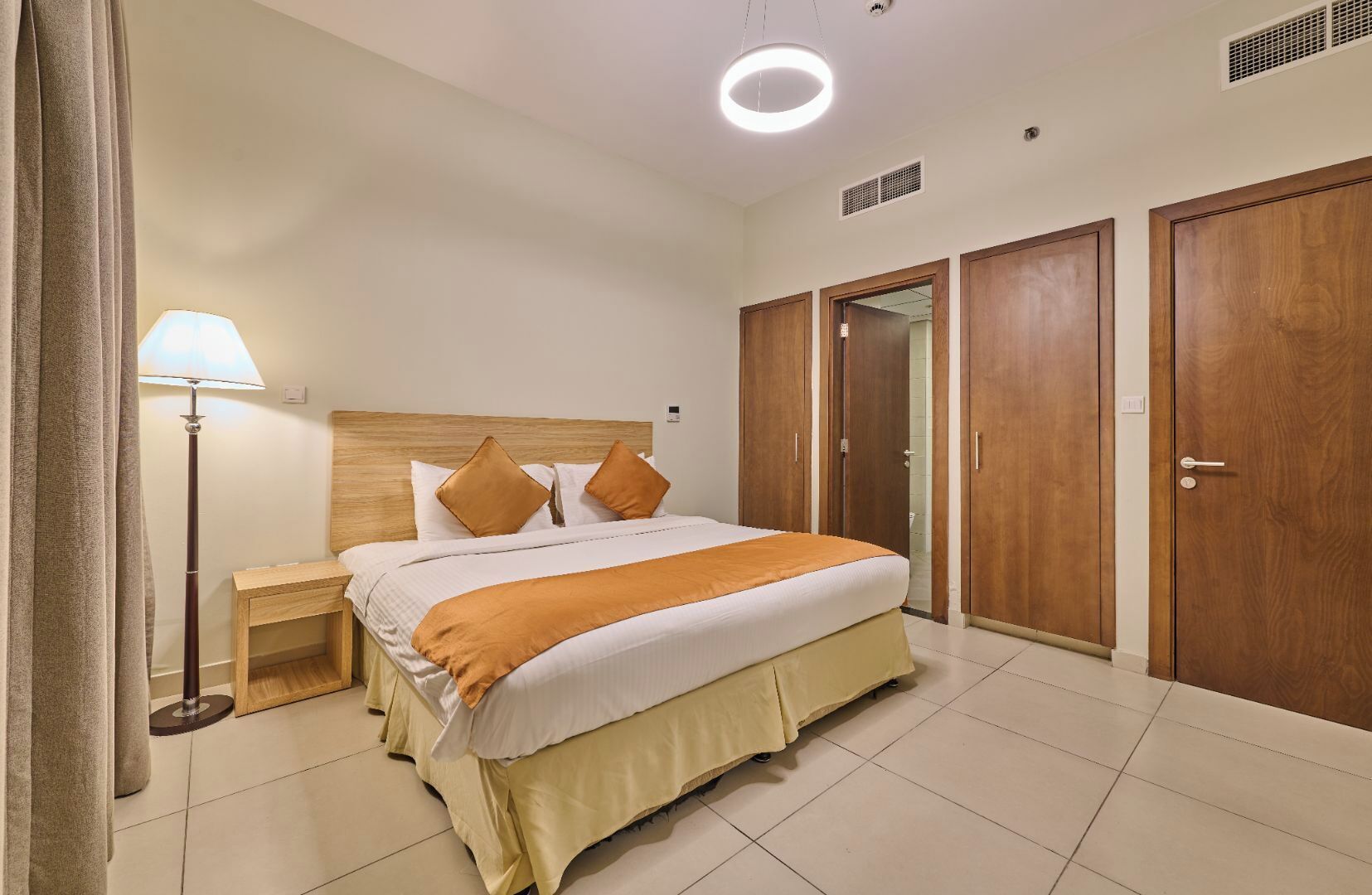 A hotel room with a bed, bedside table, lamp, wardrobe, and a ceiling light.