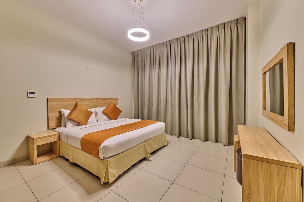 Una habitación de hotel con cama, mesitas de noche, un escritorio, un espejo y un ventanal con cortinas.