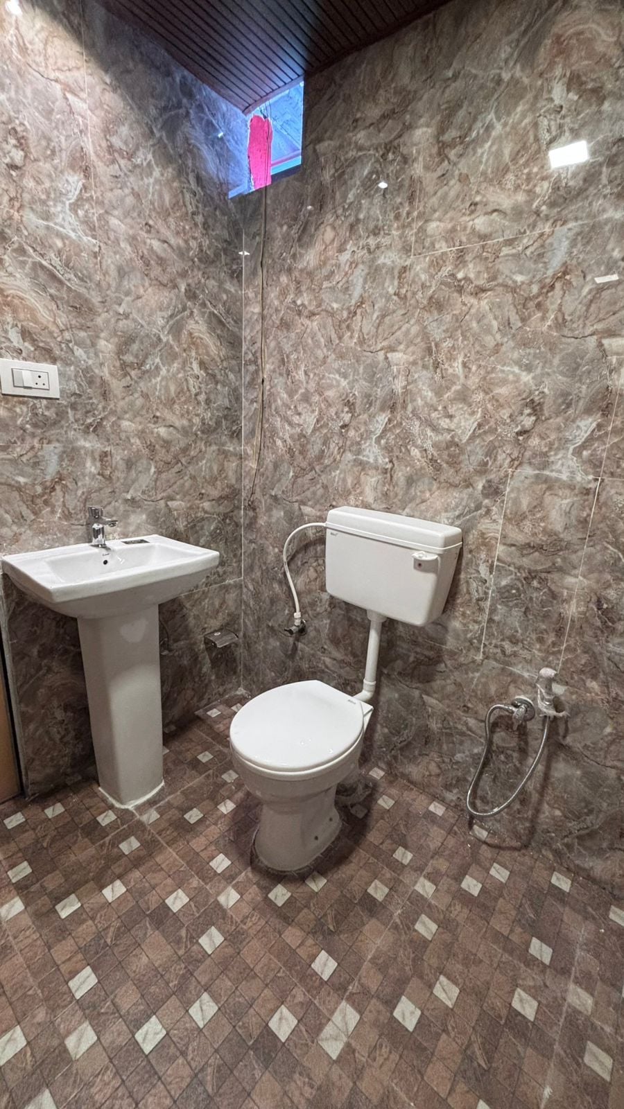 Un baño con pared de mármol, lavamanos, inodoro y ducha.