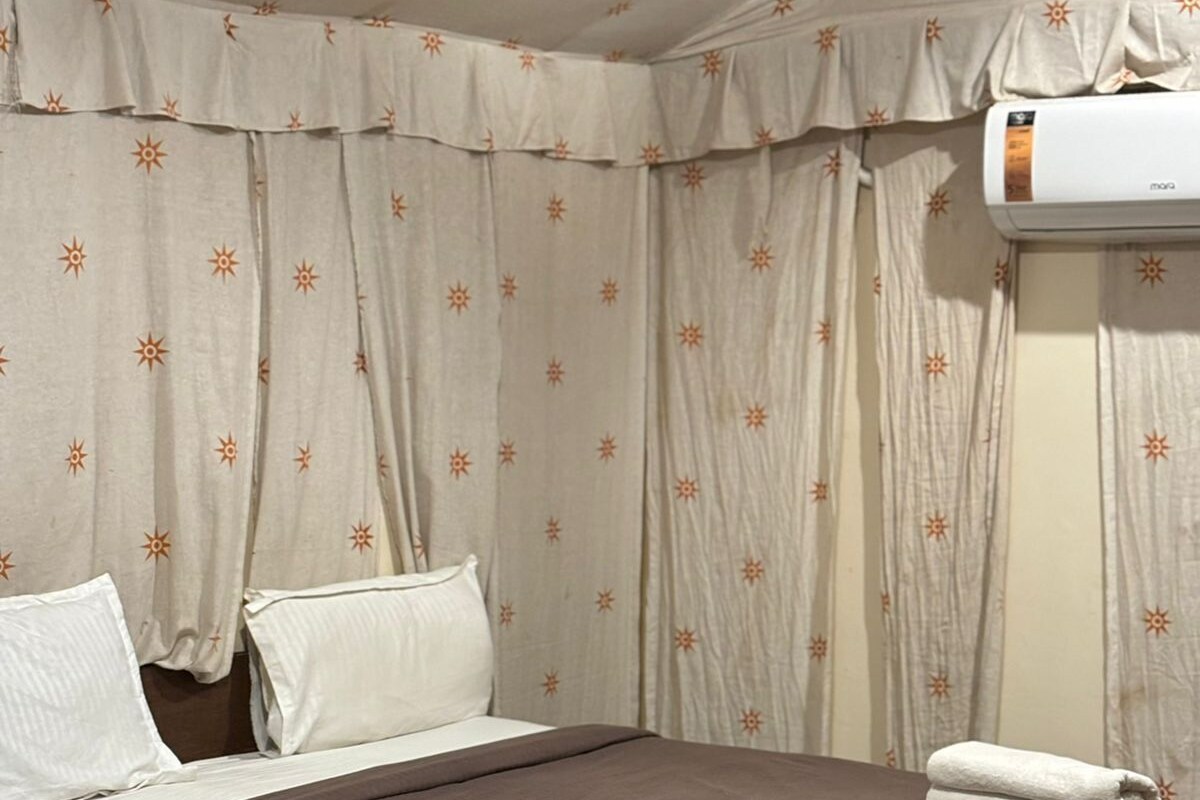 A hotel room with a bed, pillows, curtains, and an air conditioning unit.