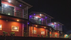 A multi-story building with balconies and windows, reflecting in a body of water. - Exotica De Swiss Panchgini (Mahabaleshwar)