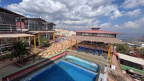 Una piscina en la azotea con sillones de descanso, una zona de juegos para niños y vistas a la ciudad.