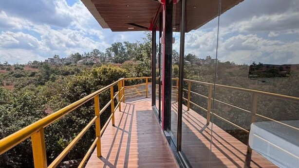 A wooden deck with glass walls, offering a view of the landscape. - Exotica De Swiss Panchgini (Mahabaleshwar)
