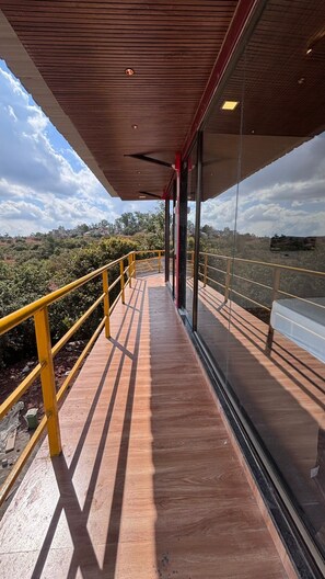 A wooden deck with glass walls, offering a view of the landscape. - Exotica De Swiss Panchgini (Mahabaleshwar)