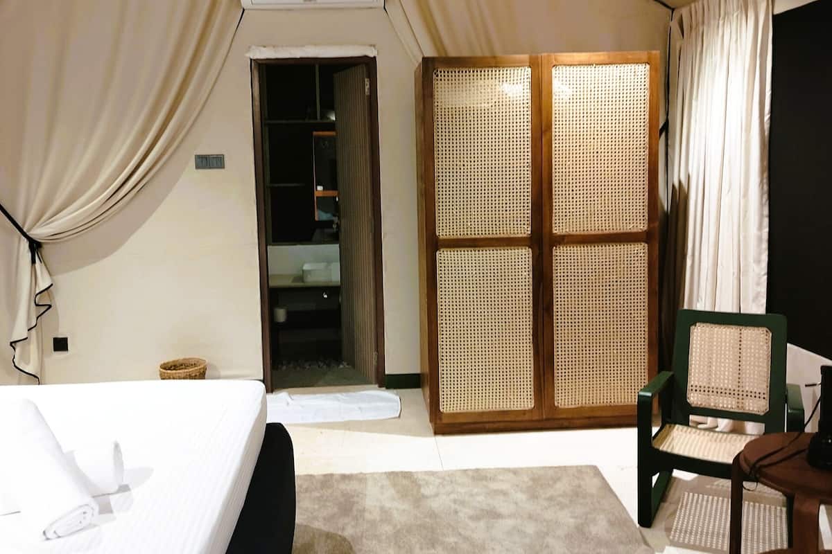Una habitación con carpa, una cama, una silla, un escritorio y una puerta que da a un baño.