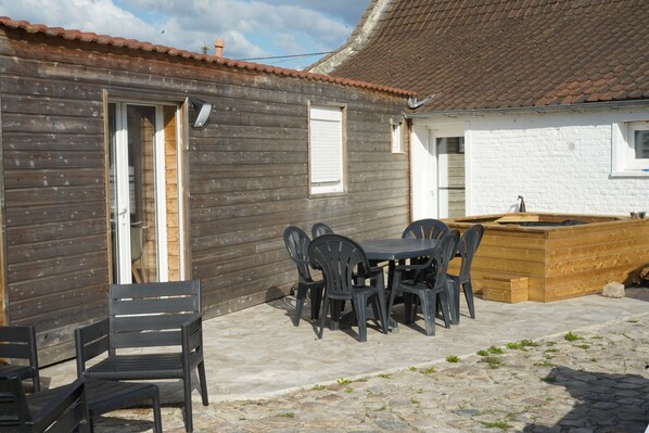 Ein Holzhaus mit Ziegeldach, einer Terrasse mit Tisch und Stühlen sowie einem Holz-Pflanzkasten.