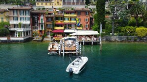 A waterfront property with a dock, boats, and colorful buildings in the background. - Baia d'oro (Gargnano)