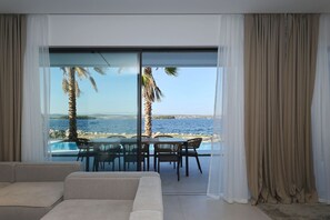 A modern living room with a large glass door leading to a balcony overlooking a body of water and palm trees. - The Palms Resort Villa Waterfront with Pool (Tkon)