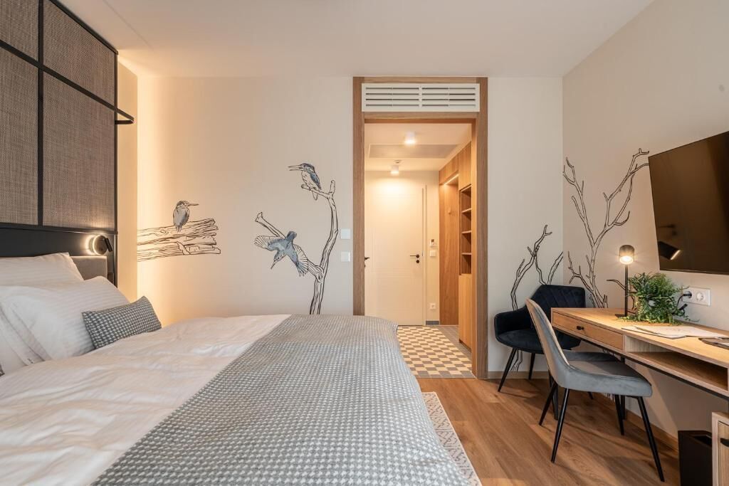 A modern bedroom with a bed, a desk, and a chair. There are wall art pieces of birds on branches.