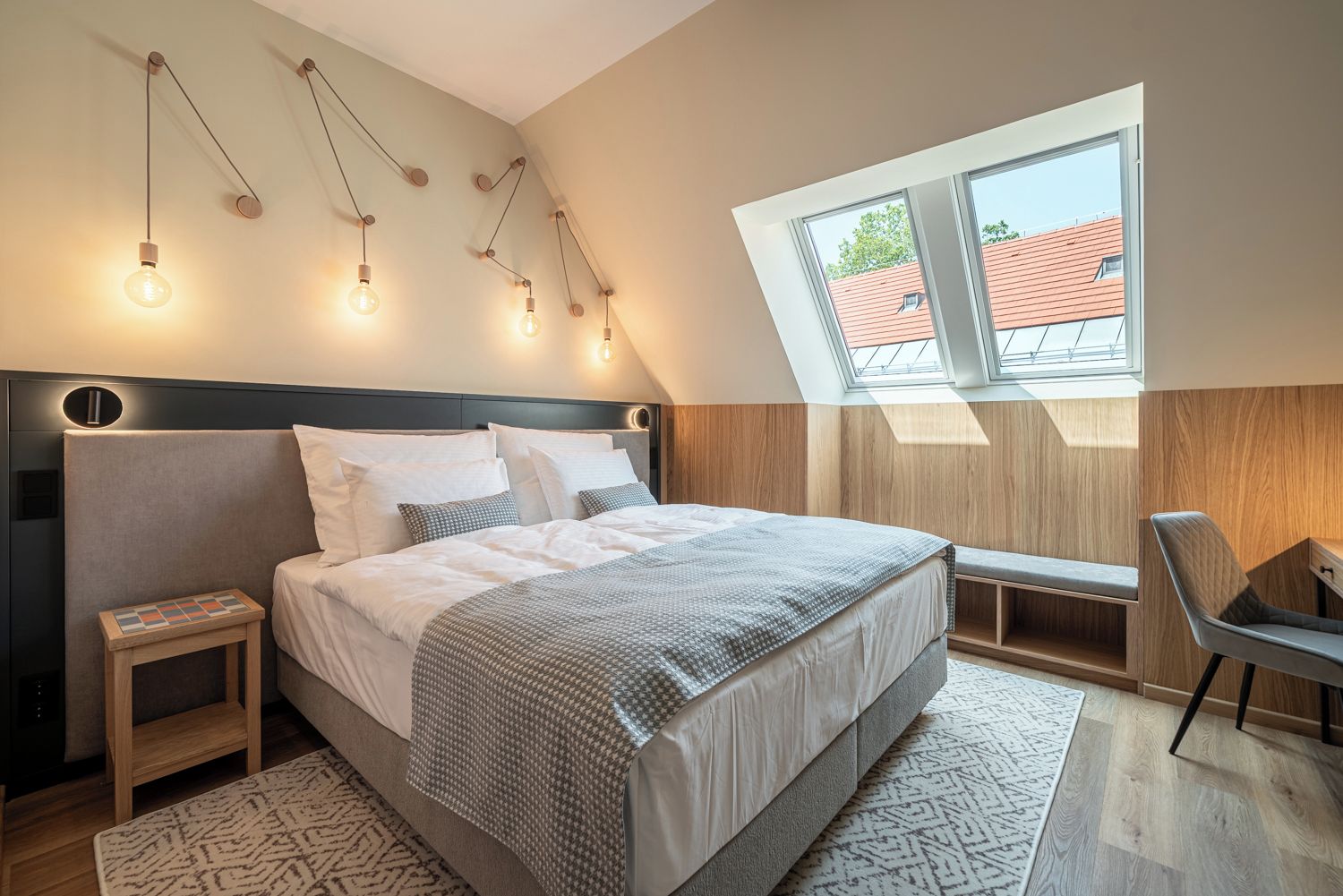 A modern bedroom with a large bed, bedside tables, a bench, and a skylight.