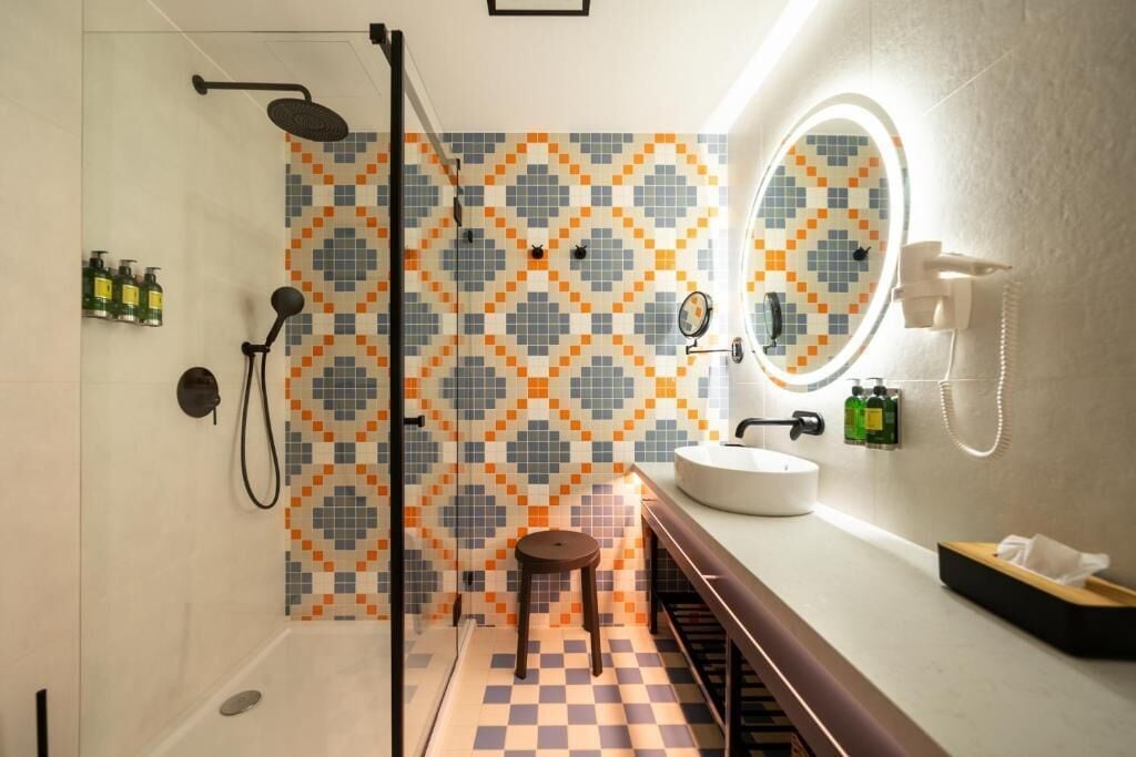 A modern bathroom with a shower, a sink, a mirror, and a patterned tile wall.