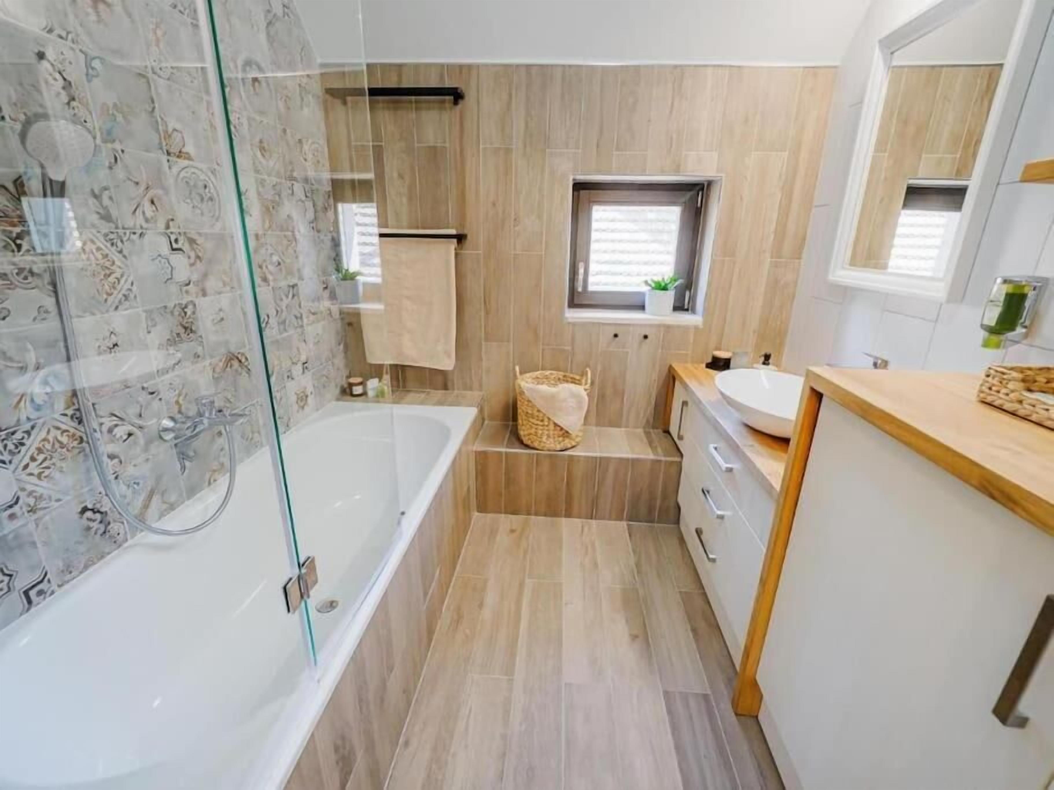 A modern bathroom with a glass-enclosed shower, a freestanding bathtub, a small window, and a vanity with a sink.