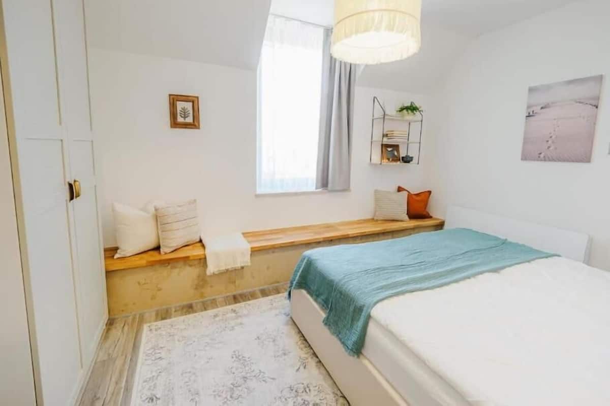 A bedroom with a bed, a window, a shelf with plants, and a door.