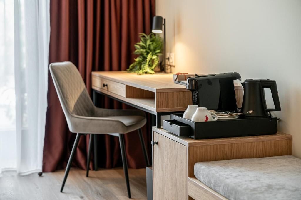 Habitación de hotel pequeña con escritorio de madera, una silla, cama, cafetera y una planta.