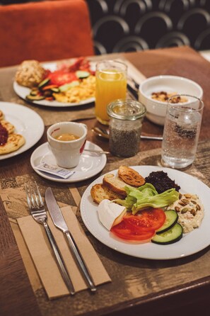 Une table mise pour le petit-déjeuner, avec des assiettes remplies de nourriture, un verre de jus d’orange et une tasse de café.