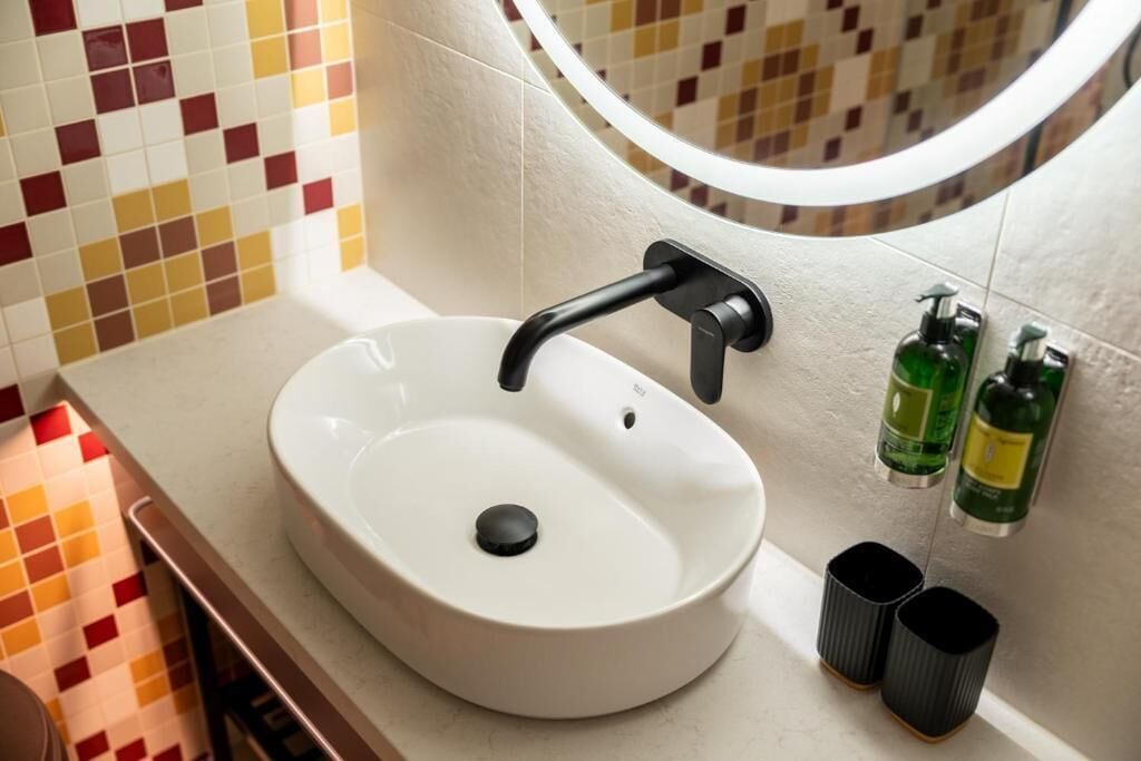 A bathroom with a white sink, a round mirror, and two green bottles on the wall.
