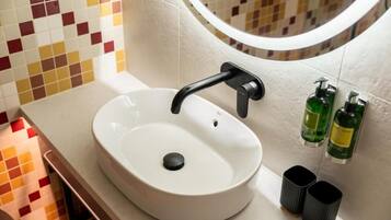 A bathroom with a white sink, a round mirror, and two green bottles on the wall.