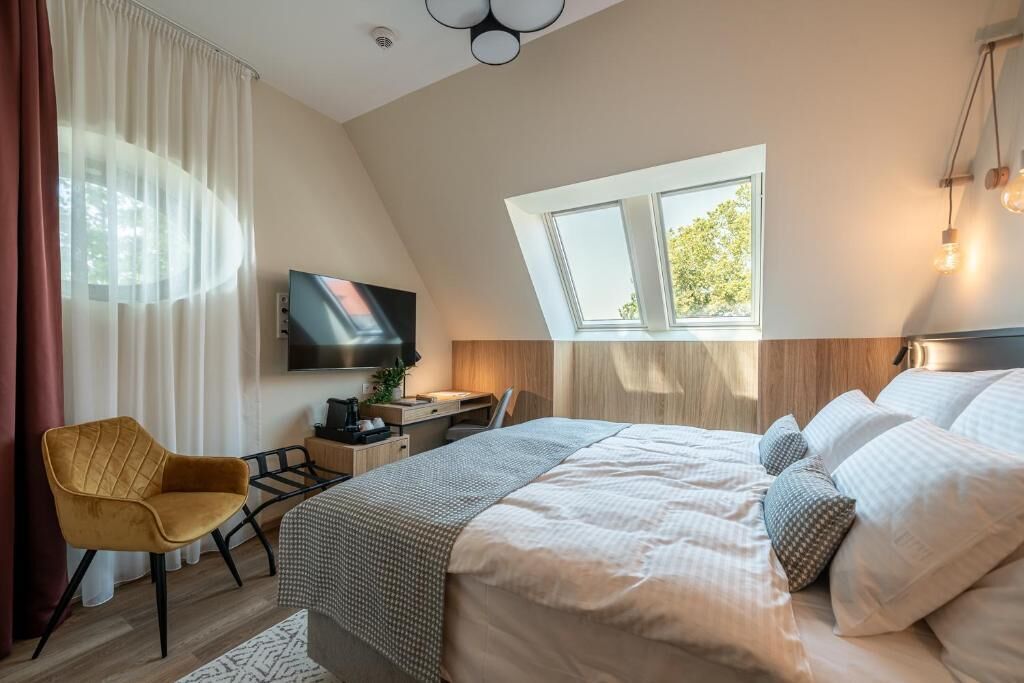A modern bedroom with a large bed, a desk, a chair, a TV, and a window.